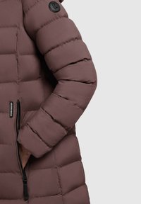 Polstret frakke i mauve med en glat tekstur, der har vandret syninger, en lynlåslomme og et rundt sort logo-patch på skulderen.