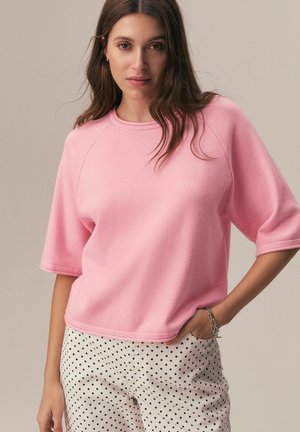 Pink fleece sweatshirt with short, raglan sleeves and round neckline, paired with polka dot pants. Soft texture with a casual fit.