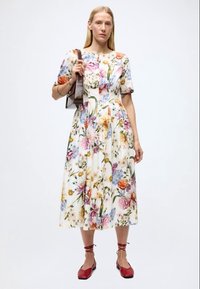 Midi-kjole med blomsterprint i let stof, med korte ærmer og en tætsiddende overdel. Fremhævet med en rund halsudskæring og et luftigt skørt.