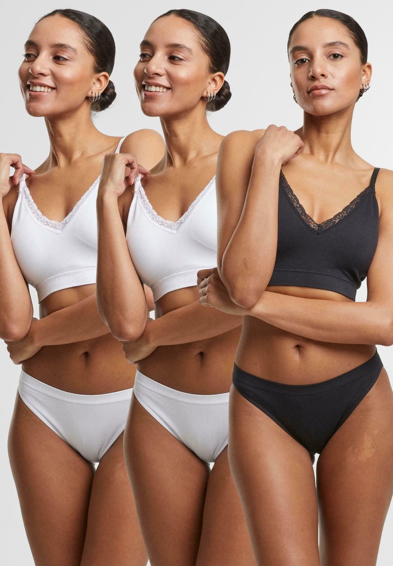 Tre set di lingerie esposti: un reggiseno bianco con rifiniture in pizzo, un reggiseno nero con pizzo e slip coordinati, tutti con una texture a coste.