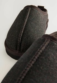 Sötétbarna vászonnadrág cipők párja, látható varrással és textúrált halszálkás mintával, világos háttér előtt.