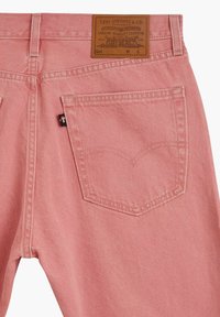 Jeans en denim rose avec une patte en cuir marron à la taille, des poches arrière avec des détails cousus et une petite étiquette de marque.