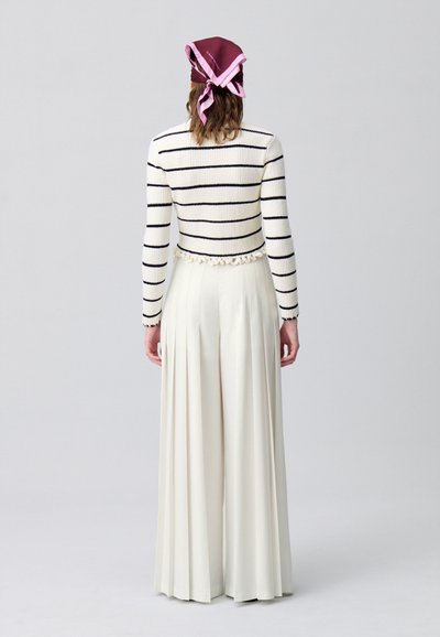 Suéter de punto a rayas en crema y negro, combinado con pantalones de tiro alto blancos y con pliegues; presenta un dobladillo con volantes y una bufanda burdeos.