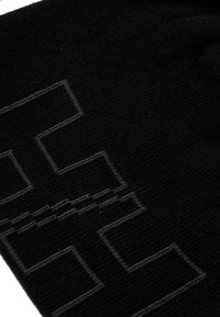 Zwarte gebreide stof met een geometrisch patroon in donkers grijs. De textuur is zacht met een lichte rek. Gestikte details zijn zichtbaar.