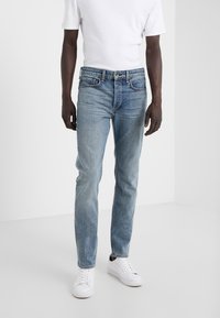 Jeans de denim azul claro con un corte recto, diseño de cinco bolsillos y cierre de botones. Llevados con una camiseta blanca y zapatillas blancas.