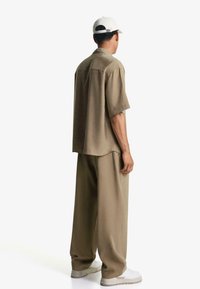 Korte mouwen khaki shirt en losse khaki broek, gecombineerd met witte sneakers en een lichte pet, gemêleerd fabric, minimalistisch ontwerp.