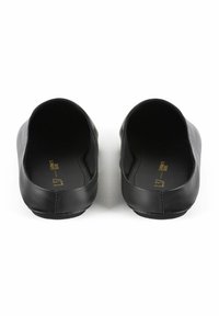 Black flat shoes with a smooth leather exterior, rounded toe, minimal design, and a flat sole, featuring subtle gold branding on the insole.