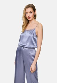 Lavendelfarbenes Seiden-Camisole mit Spitzenbesatz, kombiniert mit passenden hoch taillierten, weit geschnittenen Hosen. Glatte Textur, einfaches Design und elegante Farbe.