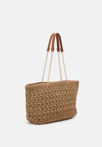 Woven taška z juty s texturovaným, béžovým povrchem, která má hnědé kožené držadla a zlaté řetízkové akcenty. Velký, otevřený design.