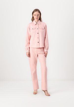Rosa denimjakke med frontlommer og knapper, sammen med matchende rosa bukser, begge har en strukturert finish. Modellen bruker sandaler med klare hæler.