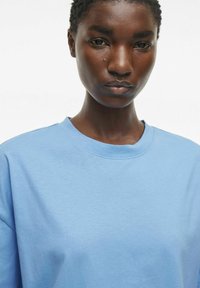 Lyseblå bomull t-skjorte med rund hals, korte ermer og en glatt tekstur, vist på en ensfarget hvit bakgrunn.