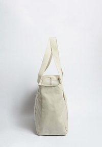 Béžová plátěná taška s texturovaným povrchem, širokými látkovými popruhy a zipovým uzávěrem na vrchu. Design má strukturovaný tvar.