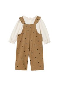 Braune Corduroy-Latzhosen mit schwarzen Herzmustern, gerüschten Schulterträgern und einer weißen Bluse mit langen Ärmeln und rundem Ausschnitt.