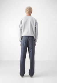 Sweat-shirt gris à manches longues associé à un pantalon large bleu, comportant des poches arrière et une texture lisse. Fond neutre.