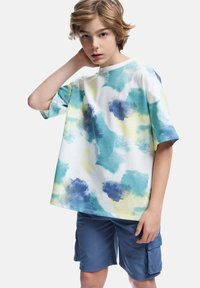 Kortærmet, løs T-shirt i hvid med et akvarelmønster i blå, grøn og gul, parret med navy cargo shorts.