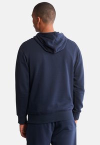 Sweat-shirt à capuche bleu marine fabriqué en tissu doux. Il présente une coupe décontractée, des poignets côtelés et une poche kangourou à l'avant.