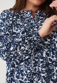 Witte blouse met een marineblauw bloemenpatroon, voorzien van een geraffineerde ronde halslijn en lange mouwen met elastische cuffs. Soepele stoftextuur.