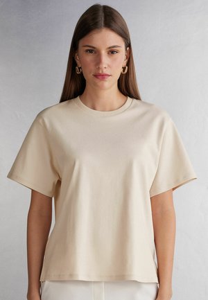 Beige katoenen T-shirt met korte mouwen, ronde hals, een relaxed fit en een gladde textuur, gepresenteerd tegen een neutrale achtergrond.