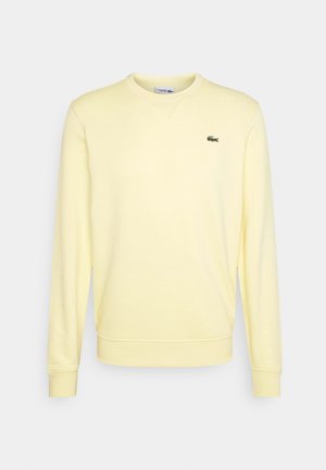 Żółta bluza z bawełny z okrągłym dekoltem, ściągaczami przy rękawach i u dołu. Posiada małe zielone logo krokodyla na klatce piersiowej.