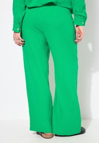 Pantalons larges verts en tissu texturé, dotés d'une coupe ample et d'un ourlet qui atteint les chevilles, associés à des chaussures noires.