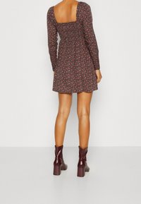 Robe mini à fleurs sombres avec des manches longues, un dos carré et une taille cintrée. Associée à des bottines à talons bordeaux. Texture lisse.