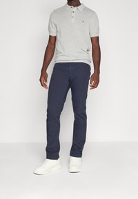 Grå stickad polo med korta ärmar, tvåknapps-stängning och en logotyp. Matchad med marinblå byxor och vita sneakers.