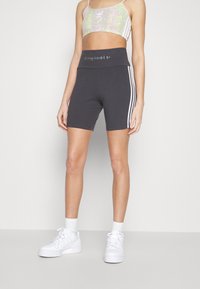 Grå sportsshorts med sidestriper, høy midje, og "originals" trykket på. Sammen med en letmønstret crop top og hvite joggesko.