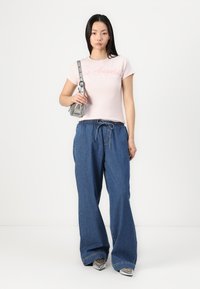Ljusrosa t-shirt med korta ärmar som har texten "Los Angeles"; lösa blå denimbyxor med snörning; liten metallisk handväska; silverfärgade skor.