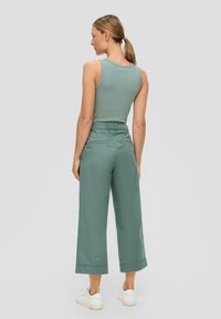 Groen geribbelde tanktop en wijde, cropped broeken in een bijpassende tint. De outfit bevat witte sneakers en heeft subtiele achterzakken.