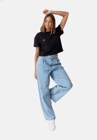 Czarna krótka koszulka z pomarańczowymi akcentami, zestawiona z jasnoniebieskimi dżinsami o wysokim stanie i szerokimi nogawkami oraz białymi trampkami. Jednolity tło.