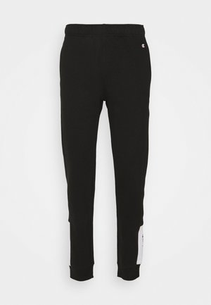 Mustat kapenevat verkkarit, joissa on joustava vyötärönauha, resoroidut nilkkasukat ja pieni Championin logo oikean taskun lähellä.