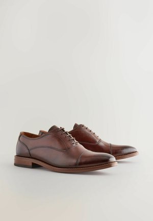 Zapatos de vestir de cuero marrón con puntera redondeada, diseño de cordones y costuras en contraste. Presentan una textura suave y un tacón bajo apilado.