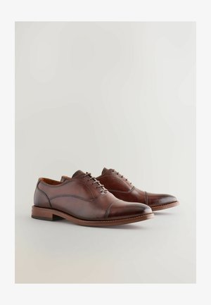 Zapatos de vestir de cuero marrón con puntera redondeada, diseño de cordones y costuras en contraste. Presentan una textura suave y un tacón bajo apilado.