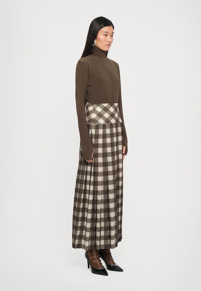 Top marrón de manga larga con cuello alto, combinado con una falda maxi a cuadros en tonos marrones y beige, con pliegues y cintura ajustada.