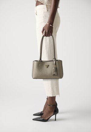 Metallic gold handbag with dual handles, textured surface, and a tag. Worn with white frayed jeans and black pointed-toe heels.
