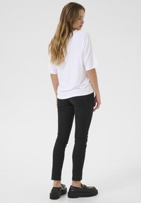 Haut blanc à manches courtes avec un ourlet arrondi, associé à un jean noir ajusté et des chaussures à plateforme noires, vu de dos.