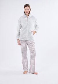 Chaqueta de forro polar con cremallera en gris claro, con un cuello alto y bolsillos, combinada con unos pantalones de pijama grises con lunares rojos.