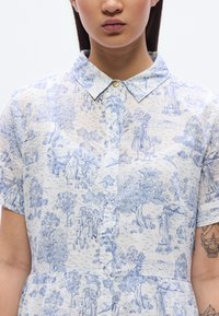 Πουκάμισο με κουμπιά από ελαφρύ ύφασμα, διακοσμημένο με αγροτικό μοτίβο σε μπλε και λευκό χρώμα με δέντρα και φιγούρες, γιακά, κοντά μανίκια και κλείσιμο με κουμπιά.