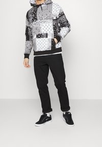 Hoodie i svart och vitt bandanamönster med dragsko i huvan, ficka fram och svarta ribbade muddar. Matcher med svarta byxor och sneakers.