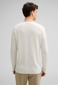 Langärmliger, Rundhalsausschnitt-Pullover in hellem Creme mit einem strukturierten Strickmuster und einer lockeren Passform, ausgestattet mit einem schlichten Saum und Ärmeln.