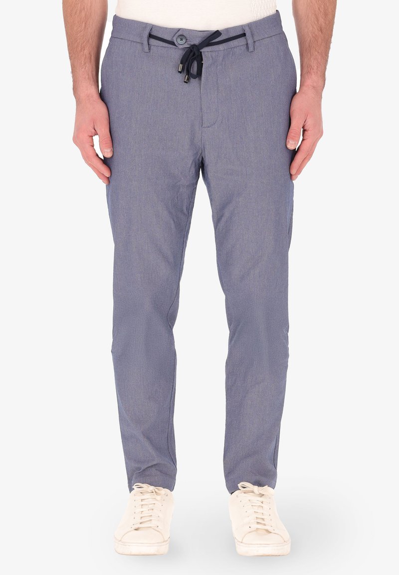 Pantaloni azzurri chiari, testurizzati, con vita a cordoncino e chiusura a bottone. Abbinati a sneaker beige, con una finitura in tessuto liscia.