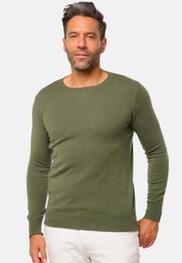 Pull vert à manches longues avec un col rond, fabriqué en matériau doux, présentant une coupe ajustée et des poignets et un ourlet côtelés.