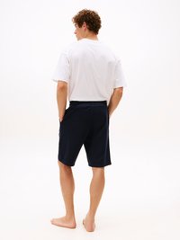 T-shirt bianca in cotone con una vestibilità rilassata, abbinata a pantaloni corti blu navy con tasche laterali e dettaglio del logo sulla gamba.