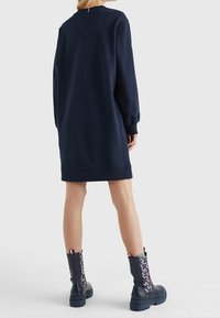 Námořnická modrá mikinová šaty s dlouhými rukávy a žebrovanými manžetami, kombinované s černými kozačkami po kolena s vzorovaným designem po stranách.