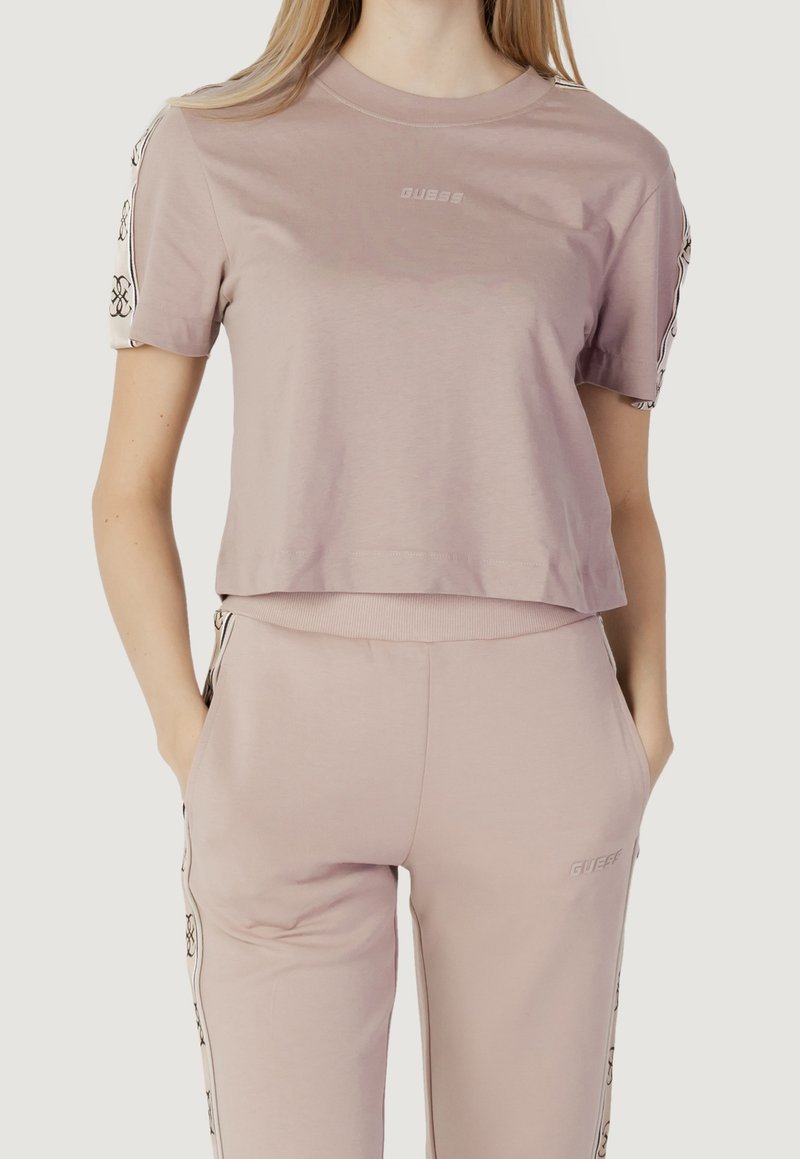 T-shirt cropped rose clair avec un col rond, présentant un impré de logo à l'avant et des accents à motifs sur les manches. Texture de tissu lisse.
