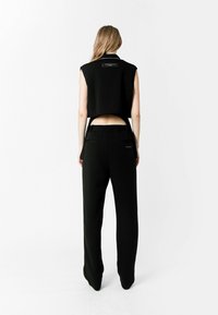 Top negro sin mangas y pantalones negros de tiro alto. La parte superior presenta un cuello y un detalle en el panel trasero. Textura suave con un ajuste entallado.