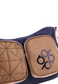 Bolso en navy y beige con diseño acolchado, que presenta dos compartimentos con cremallera y un logotipo negro en el bolsillo frontal. Textura suave en toda su superficie.