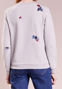 Felpa grigia con ricami floreali in rosso, blu e nero. Presenta un collo rotondo e polsini e orlo a costine. Vestibilità casual.