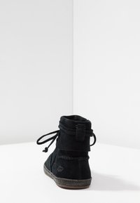 Černé semišové kotníkové boty se zaoblenou špičkou, šněrováním a texturovanou šitým podešví. Obsahují malé logo na vnější patě.