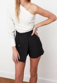 Witte off-shoulder top met een gedrapeerd ontwerp en lange mouwen, gecombineerd met hoge zwarte shorts met een geknoopte tailleband.